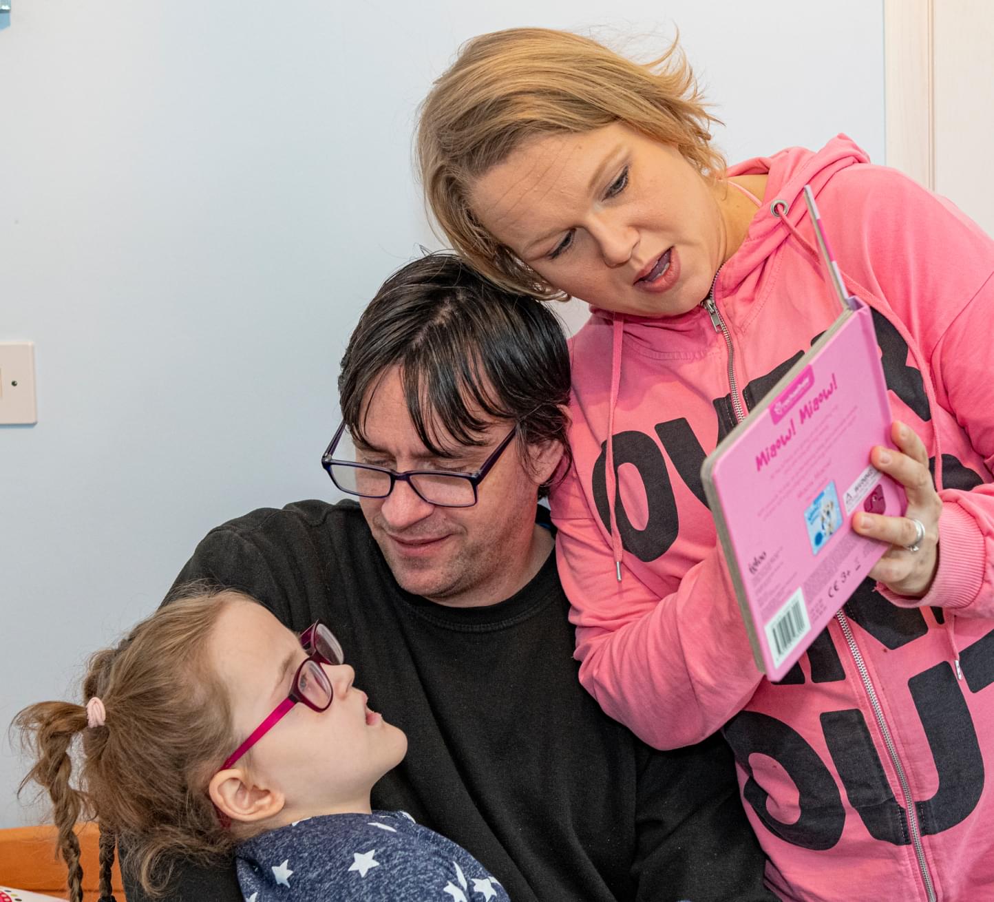 Dad Dan holds his daughter Elisa in his arms while Mum Maiju leans over and reads a book.