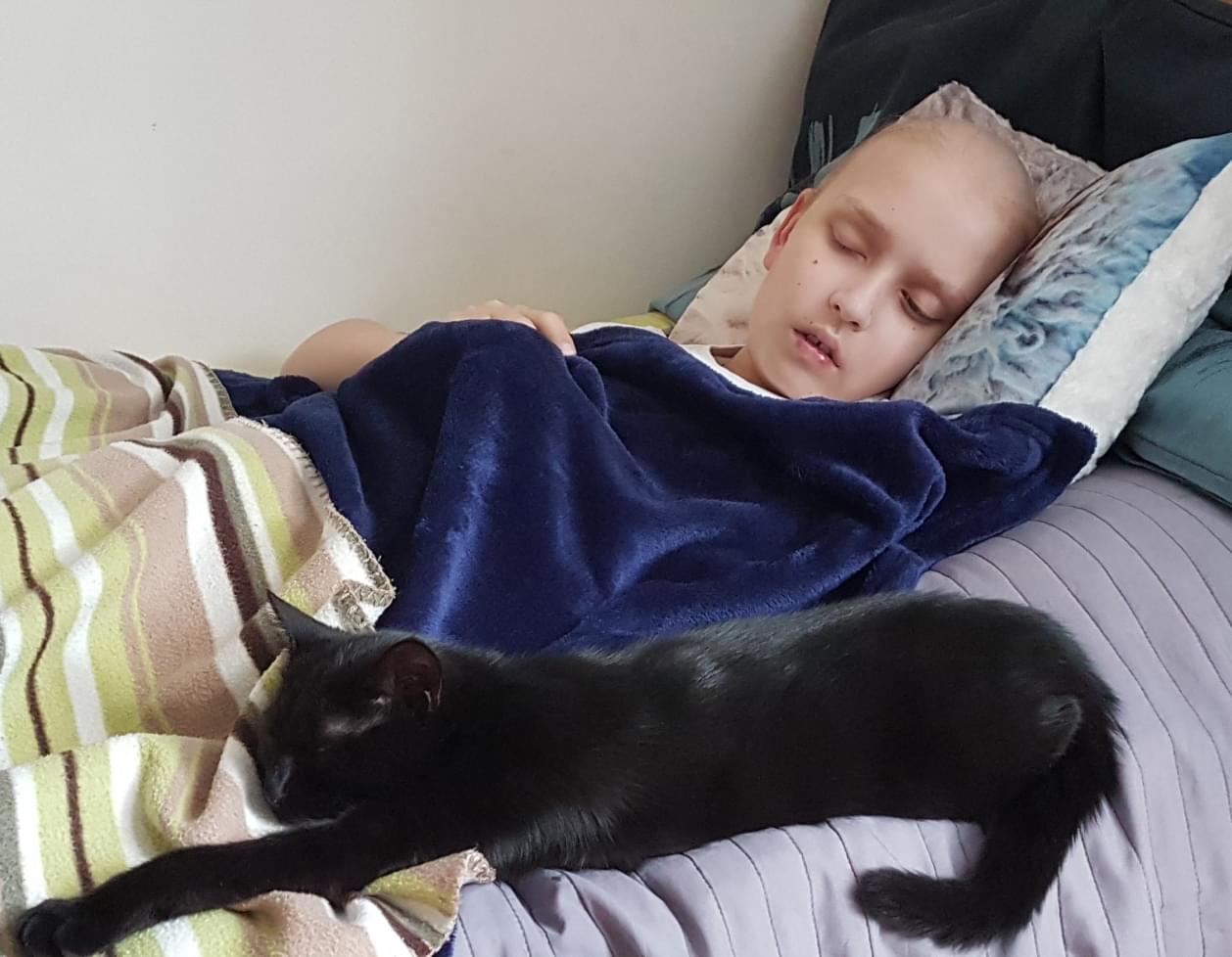 Kacper lies in bed with blankets with his cat asleep nearby.