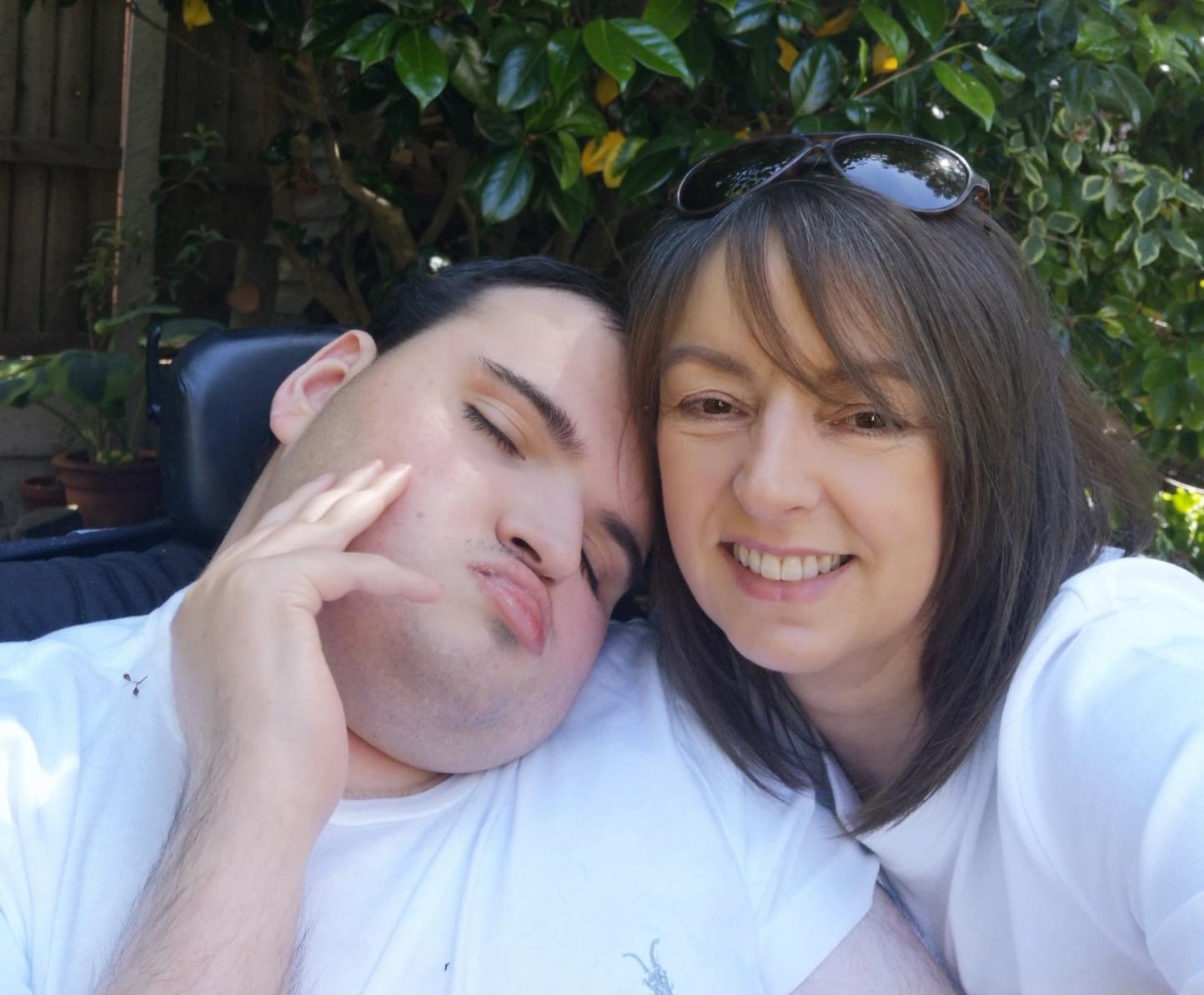 Boy in wheelchair, pictured with his mum who is holding him close.