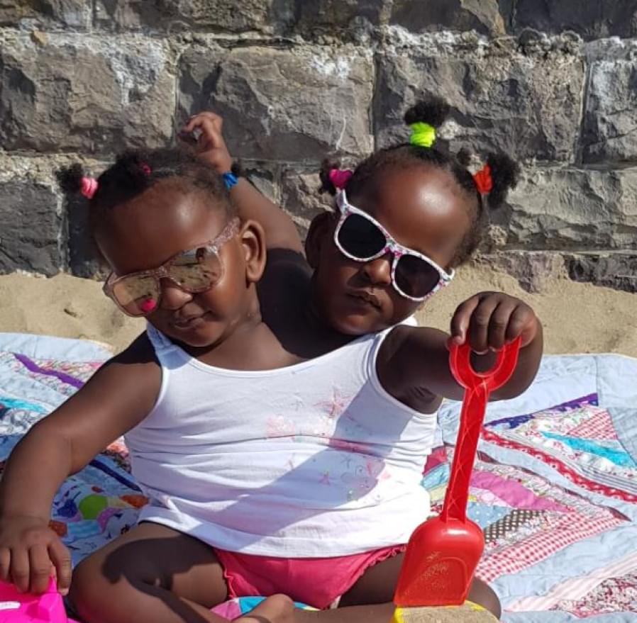 Conjoined twins Marieme and Ndeye pictured at the beach, wearing sunglasses and holding a spade.